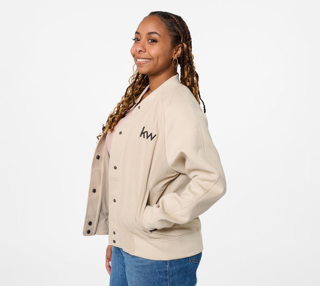 Woman wearing a beige letterman jacket with 'kw' logo on a white background