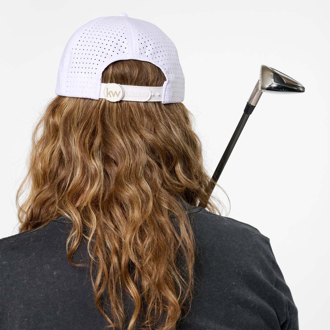 Person wearing a white cap with a logo, holding a golf club on a plain background