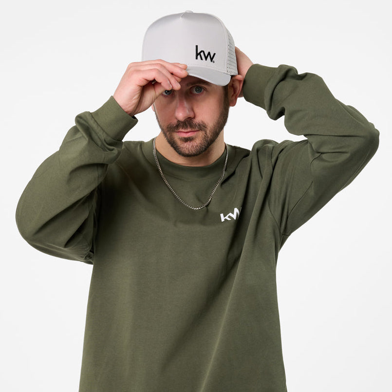 Man wearing a green long-sleeve shirt and blue jeans with a white cap on a white background