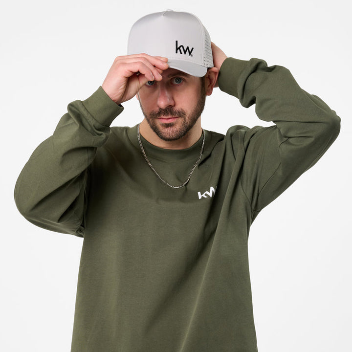 Man wearing a green long-sleeve shirt and blue jeans with a white cap on a white background