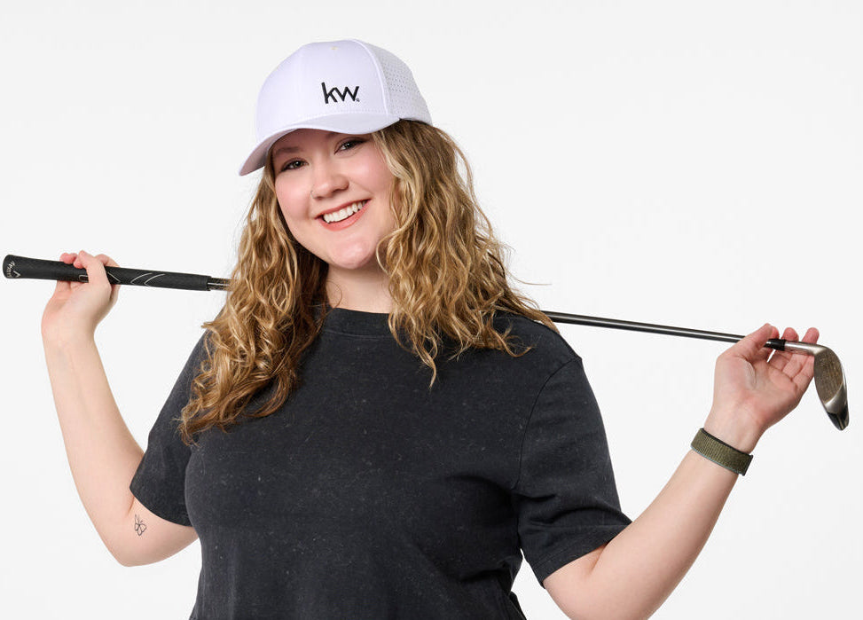 Person holding a golf club with a white cap and black shirt on a plain background