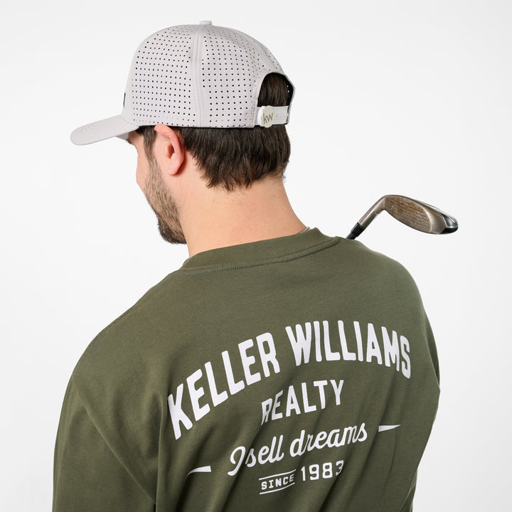 Man wearing a green 'Keller Williams Realty' shirt with a golf club on a white background