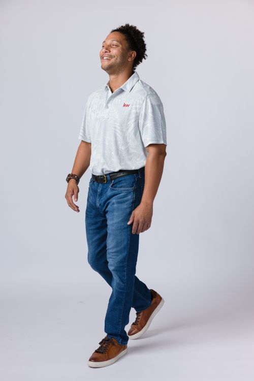 Man wearing a light gray polo shirt with a logo and blue jeans on a white background