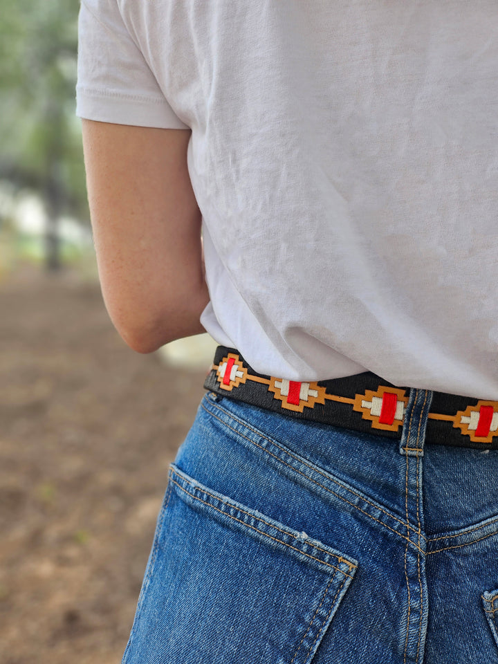 Person wearing a patterned belt with a blurred outdoor background